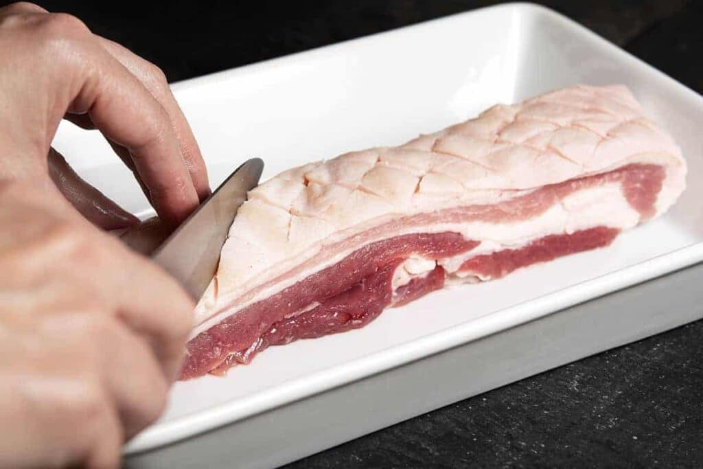 A view of a person cutting pork belly with a knife