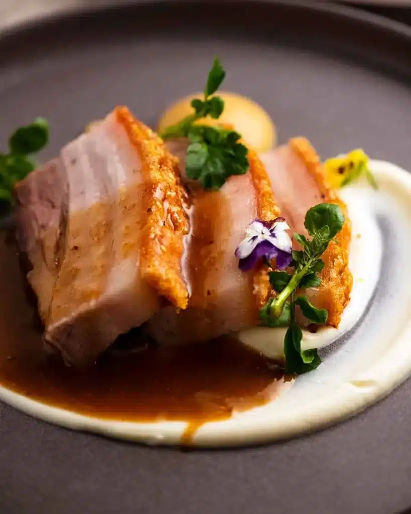 A view of a pork belly plated out with vermouth sus sauce