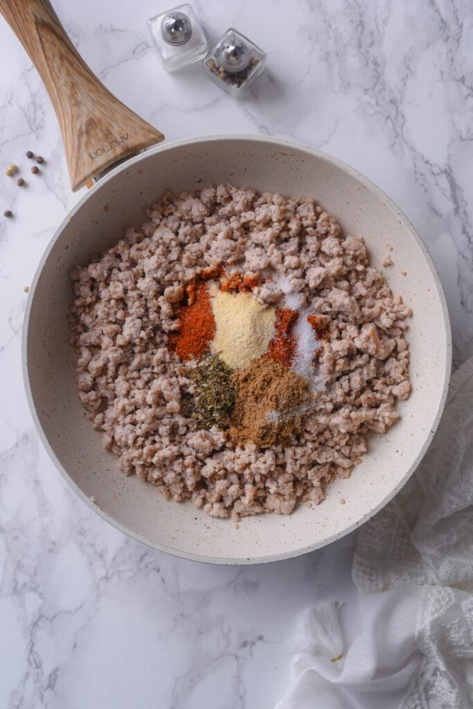 xAn overhead view of ground meat inside a pan with spices on top