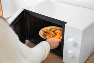 Woman Putting Plate With Fried Potato In Microwave Oven