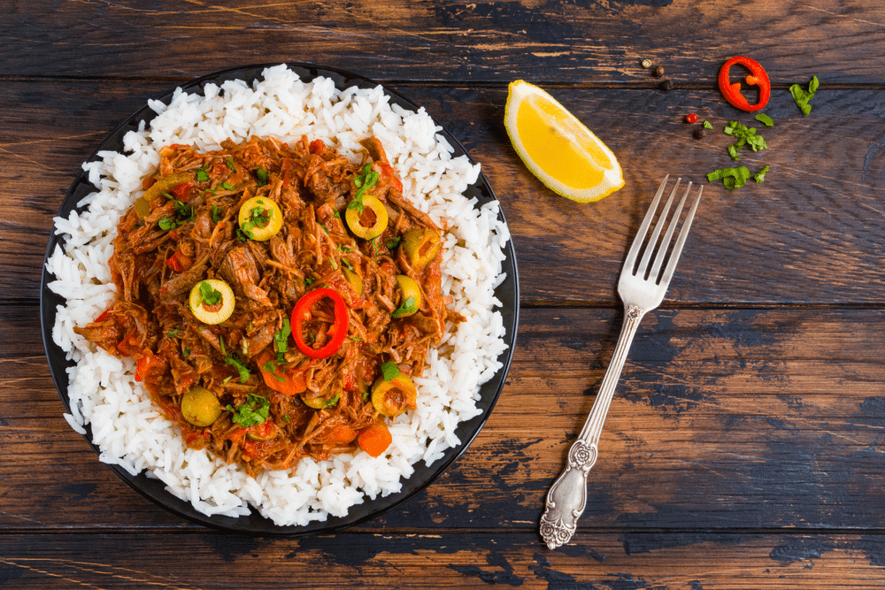 Ropa Vieja Cuban national dish stewed beef with wine and tomatoes on a black plate with a boiled rice